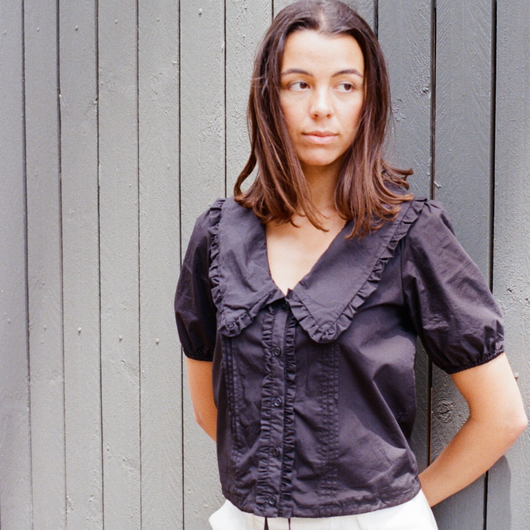 Woman wearing a dark blouse with ruffled details against a gray wooden background
